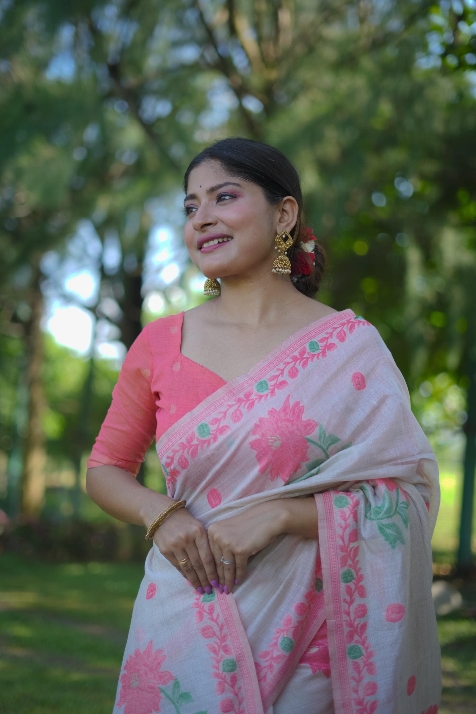Woman wearing a pink saree with resham weaving design and golden earrings