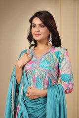 Woman wearing a colorful traditional outfit with a blue dupatta against a beige background