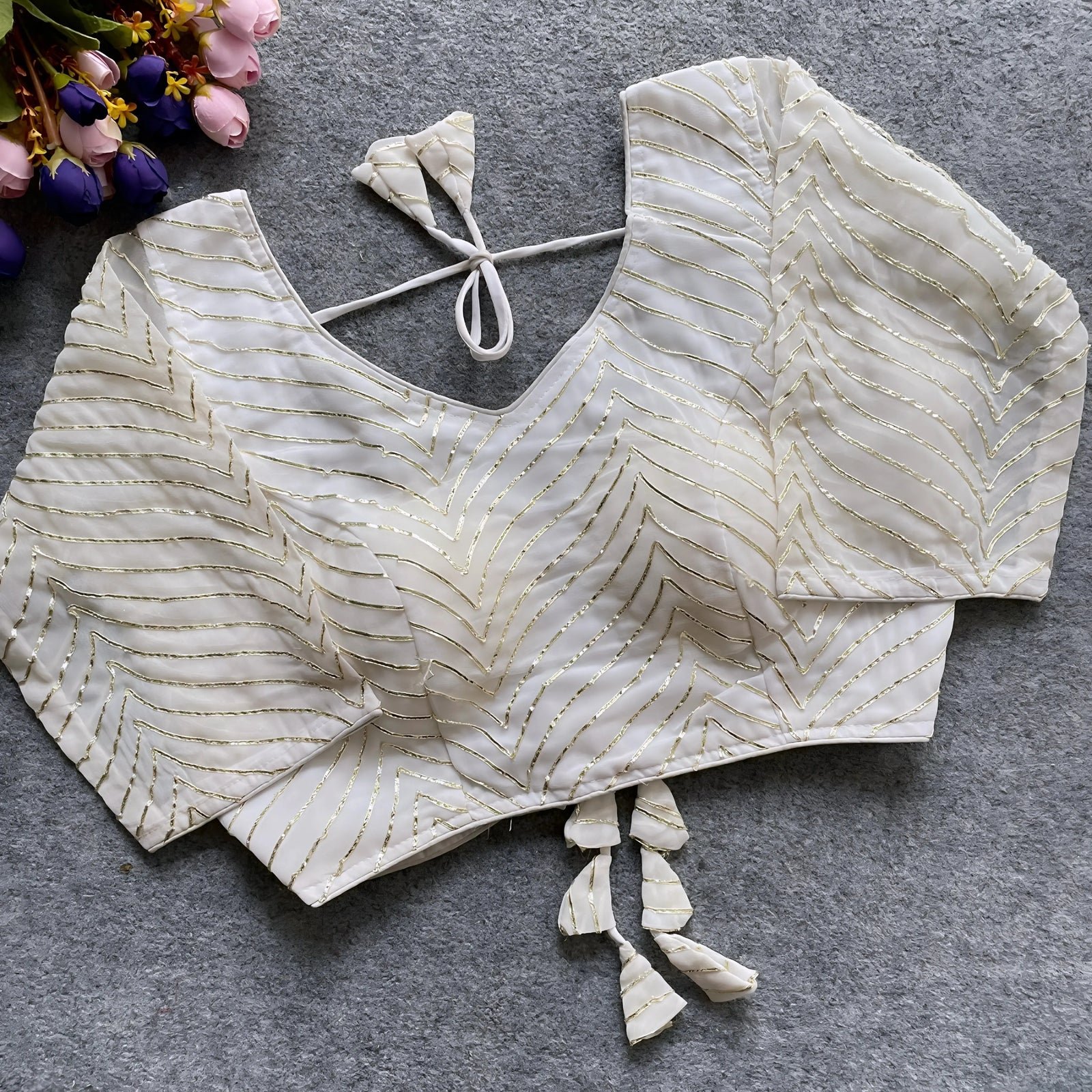 White designer blouse with golden thread embroidery, featuring a deep back neckline and decorative tassels