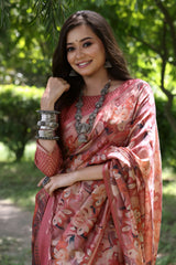 A woman models a Soft Tussar Silk Saree in a dusty maroon color, covered in an elaborate all-over artistic print. The saree has a distinct woven Zari border. She wears a matching long-sleeve blouse and an oxidized silver necklace, posing outdoors in a garden.