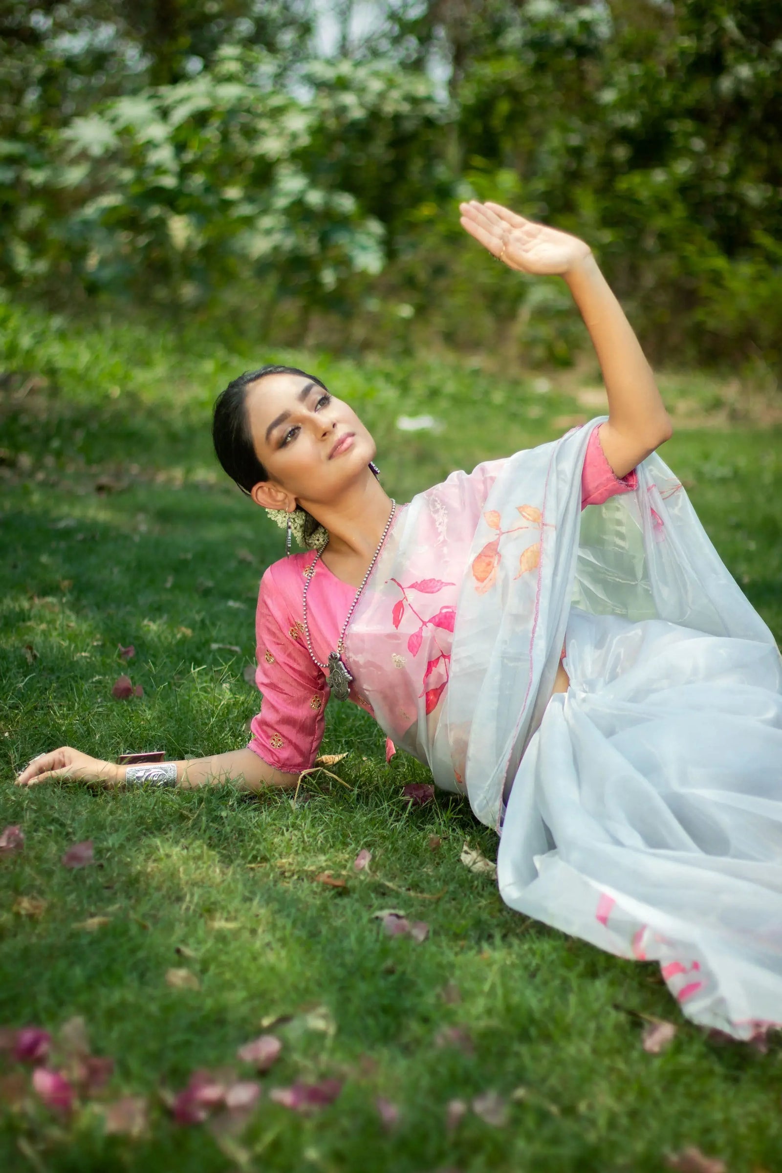 Woman wearing a white saree with intricate pattern print, lying on grass in an elegant pose