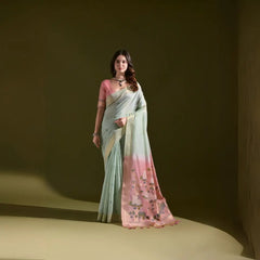 A woman models a Soft Muga Cotton Saree. The saree's body is pale sea green with a gold Zari border. The pallu dramatically transitions to a soft rose pink color featuring woven motifs. She wears a pink blouse and a dark gemstone choker necklace.