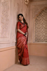 Woman wearing a maroon silk saree with intricate geometric border and pallu, paired with traditional jewelry, standing in a heritage-inspired room with ornate wall carvings and a decorative lattice window.