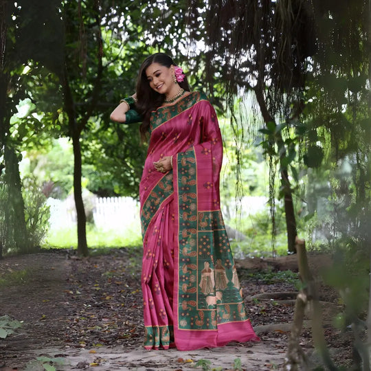 A woman models a Dark Pink Soft Tussar Silk Saree with small gold motifs. The saree has a wide, contrasting deep forest green border and pallu featuring intricate traditional and figurative prints. She wears a green blouse and is adorned with gold jewelry and a pink flower in her hair.
