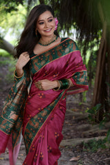 A woman models a Dark Pink Soft Tussar Silk Saree with small gold motifs. The saree has a wide, contrasting deep forest green border and pallu featuring intricate traditional and figurative prints. She wears a green blouse and is adorned with gold jewelry and a pink flower in her hair.