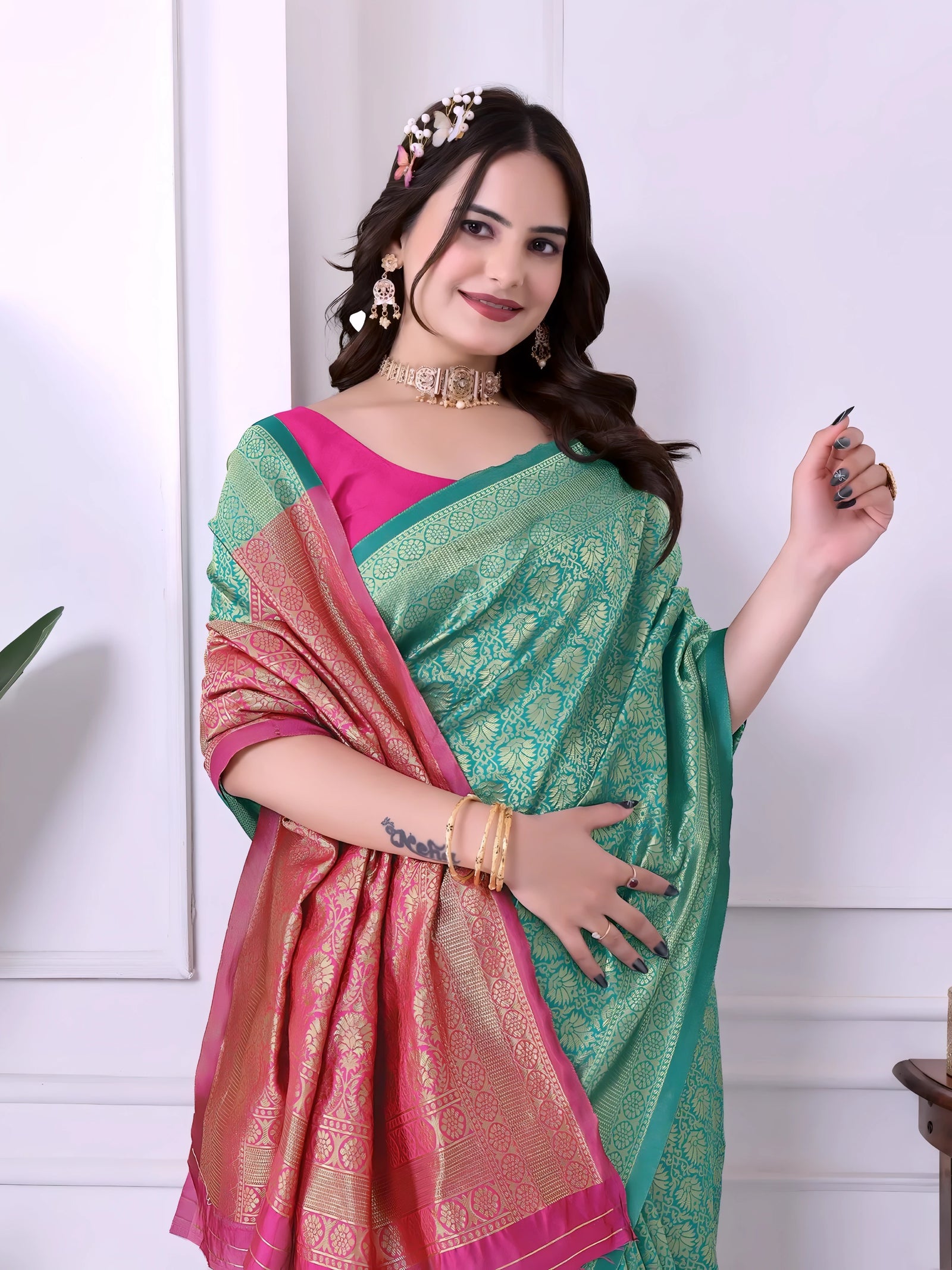 A woman models a striking Sea Green Banarasi Silk Saree with dense all-over gold Zari weaving. The pallu and border feature a dramatic contrast with hot pink. She wears a hot pink short-sleeve blouse and gold Kundan jewelry, posing indoors.