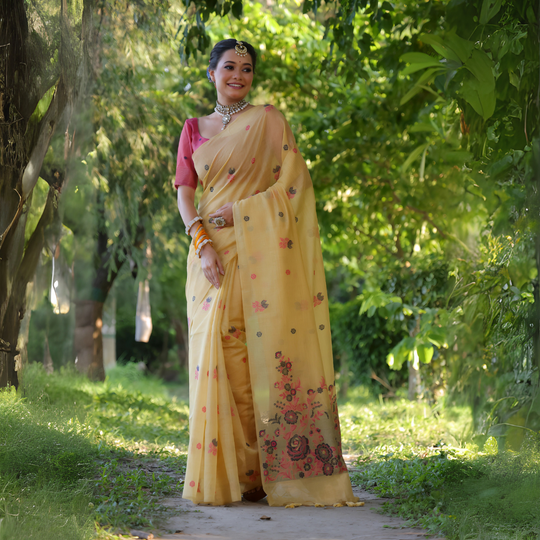 A woman models an elegant Soft Pink Silk Saree with subtle texture. The saree has a wide, shimmering gold Zari border framed by deep pink piping. The pallu is the focal point, featuring rich, artistic Paithani-style print or weaving of pink, red, and brown bird-on-branch motifs. She wears a pink sleeveless blouse and gold Kundan jewelry, posing in a white, ornate courtyard.