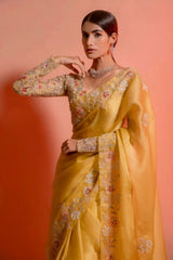 A woman models a striking Golden Yellow Soft Organza Silk Saree. The saree features delicate thread and sequin floral embroidery along the border. She wears a matching long-sleeve, heavily embroidered blouse and accessorizes with silver/diamond jewelry.