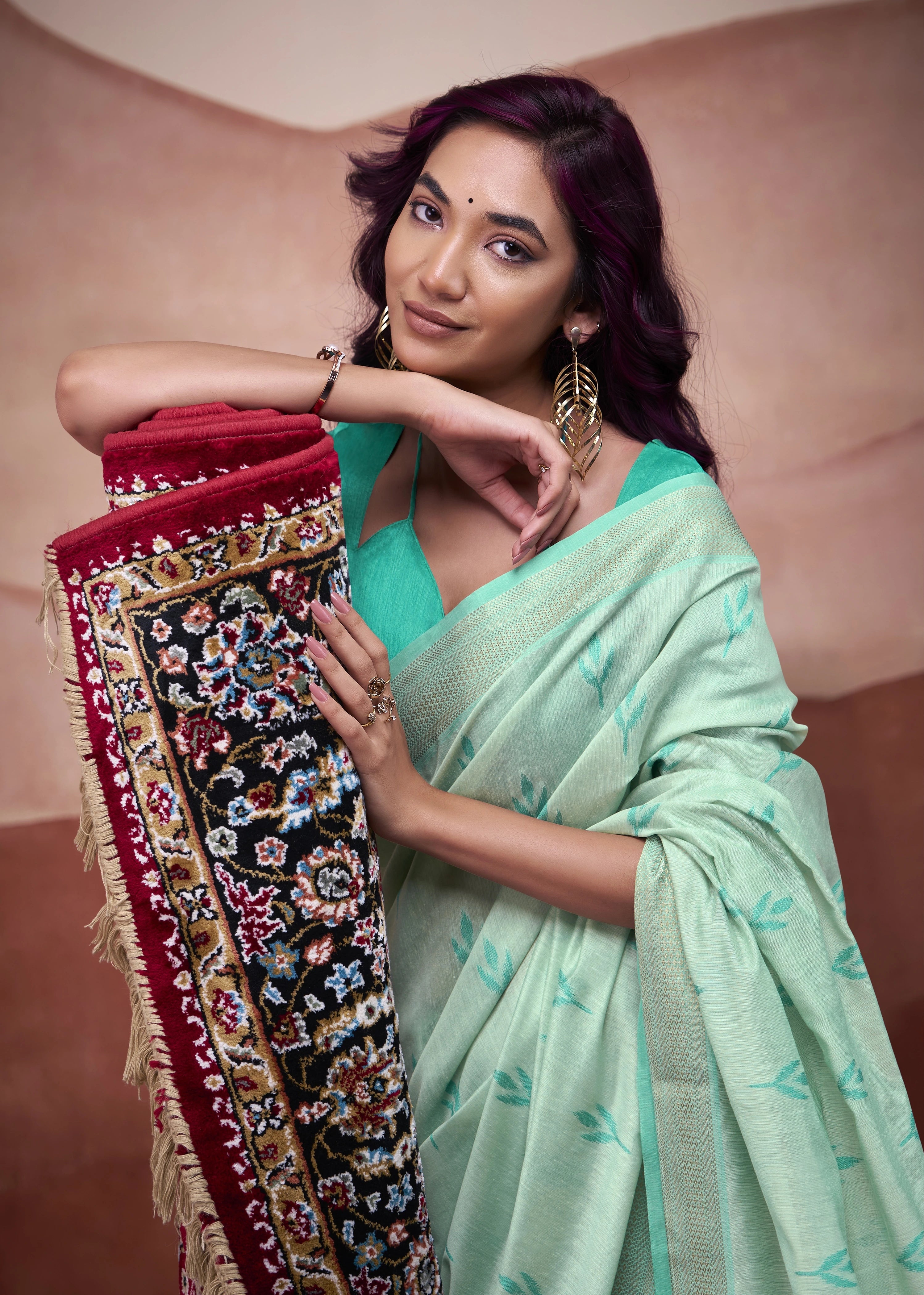 Woman in a light green saree holding a decorative fabric against a plain background