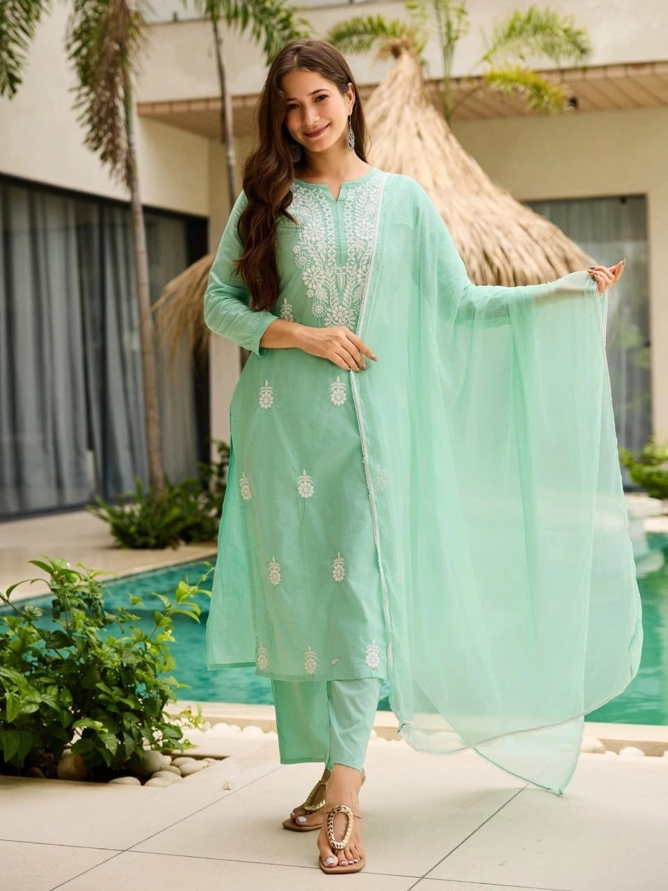 Woman in a light green traditional outfit standing by a poolside.