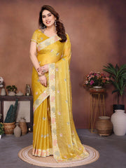 Woman wearing a yellow saree with floral patterns in an indoor setting.