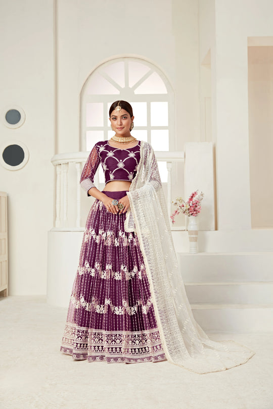 Woman in a purple traditional outfit with a white dupatta in a bright room.
