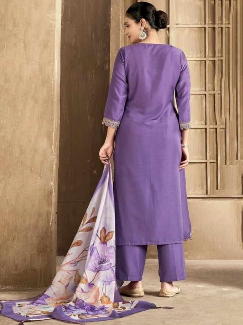 Woman in a purple traditional outfit holding a matching scarf against a beige wall.