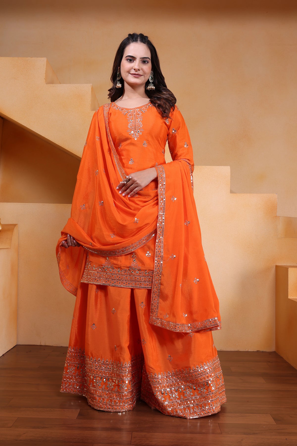 Woman in an orange traditional outfit with embroidery standing on a wooden floor.