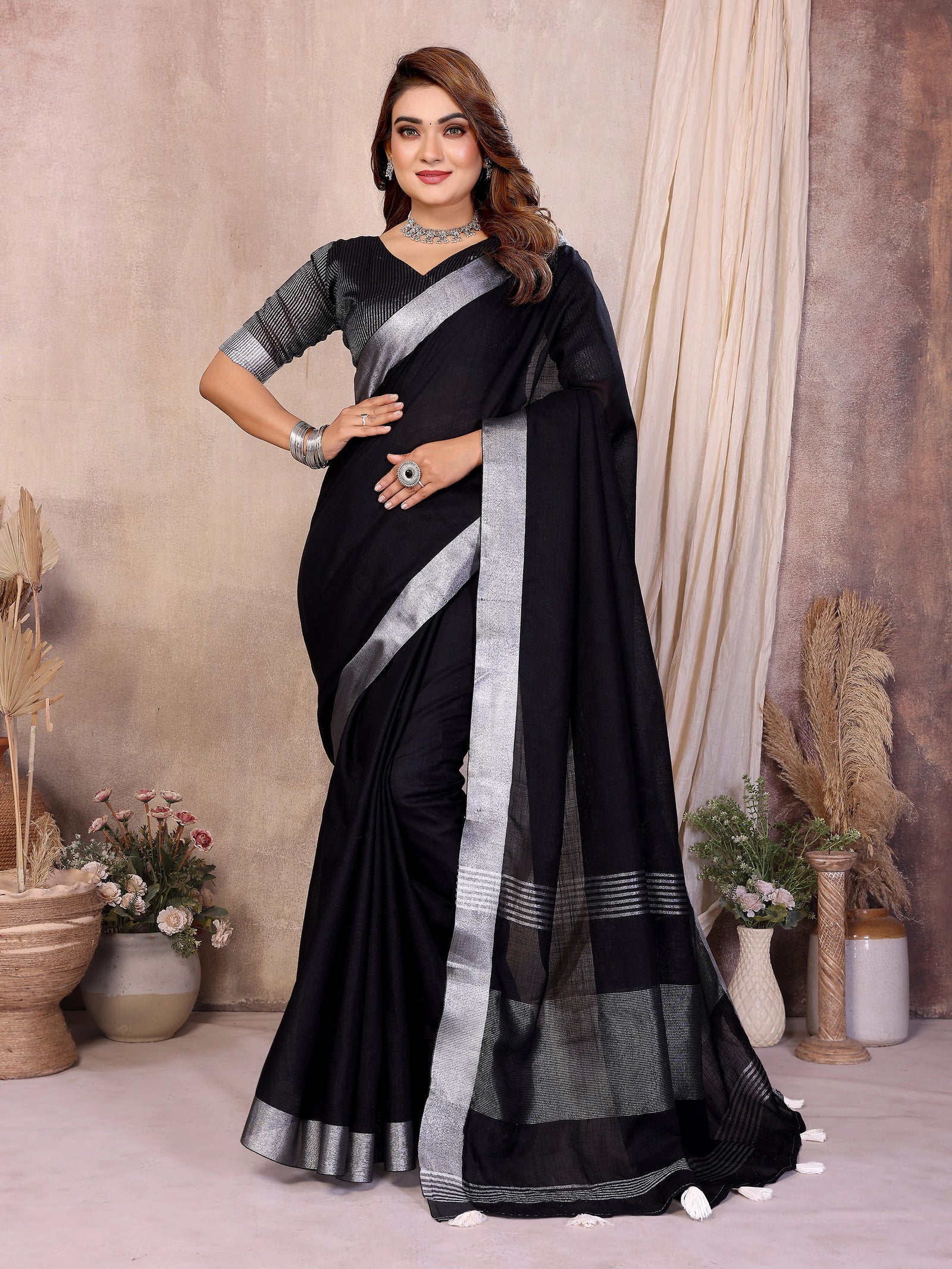Woman wearing a black saree with silver border in a decorated room.