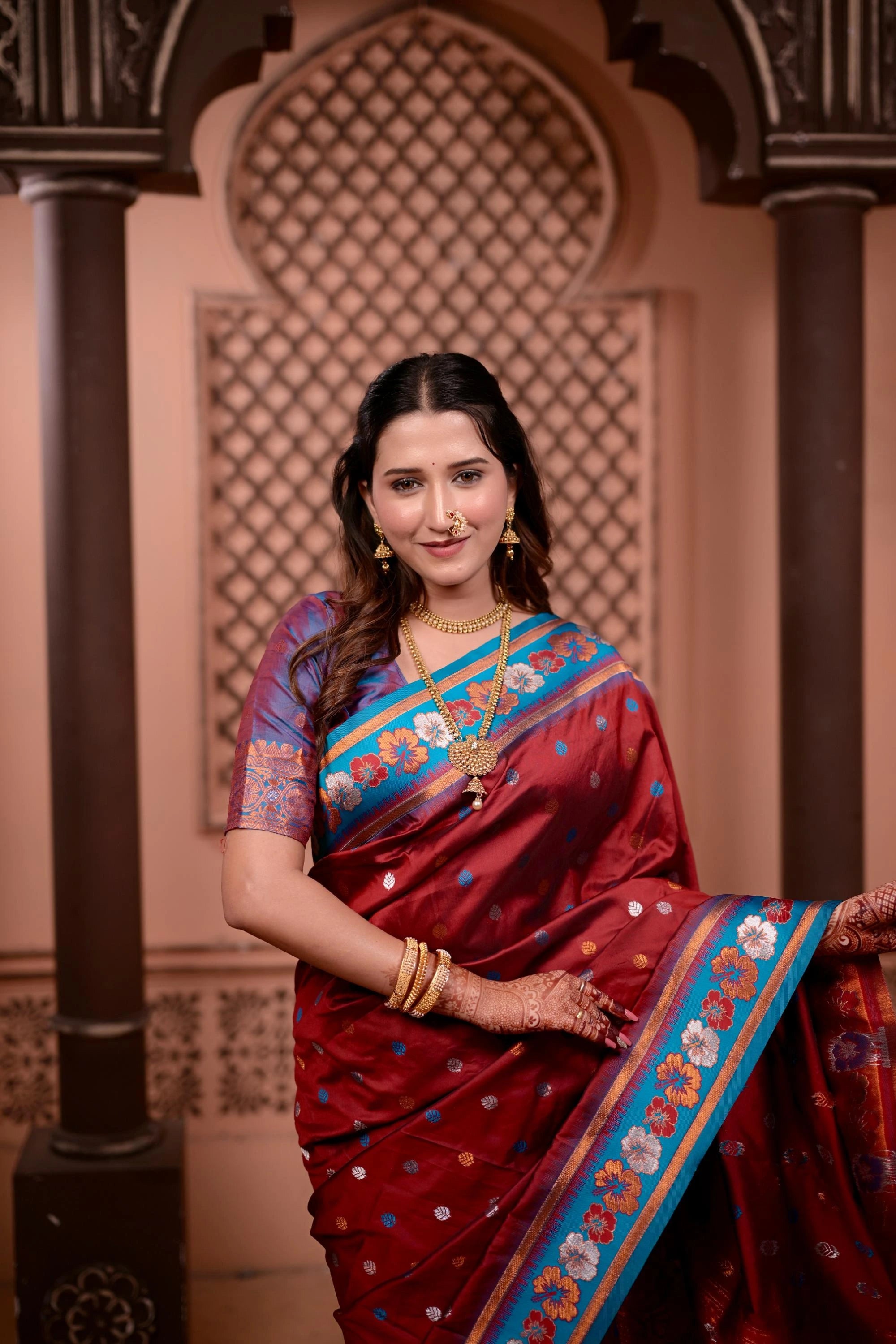 Woman in a traditional saree with decorative jewelry against an ornate architectural background
