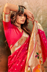 Woman in a red saree with gold border holding a matching saree against a textured wall.
