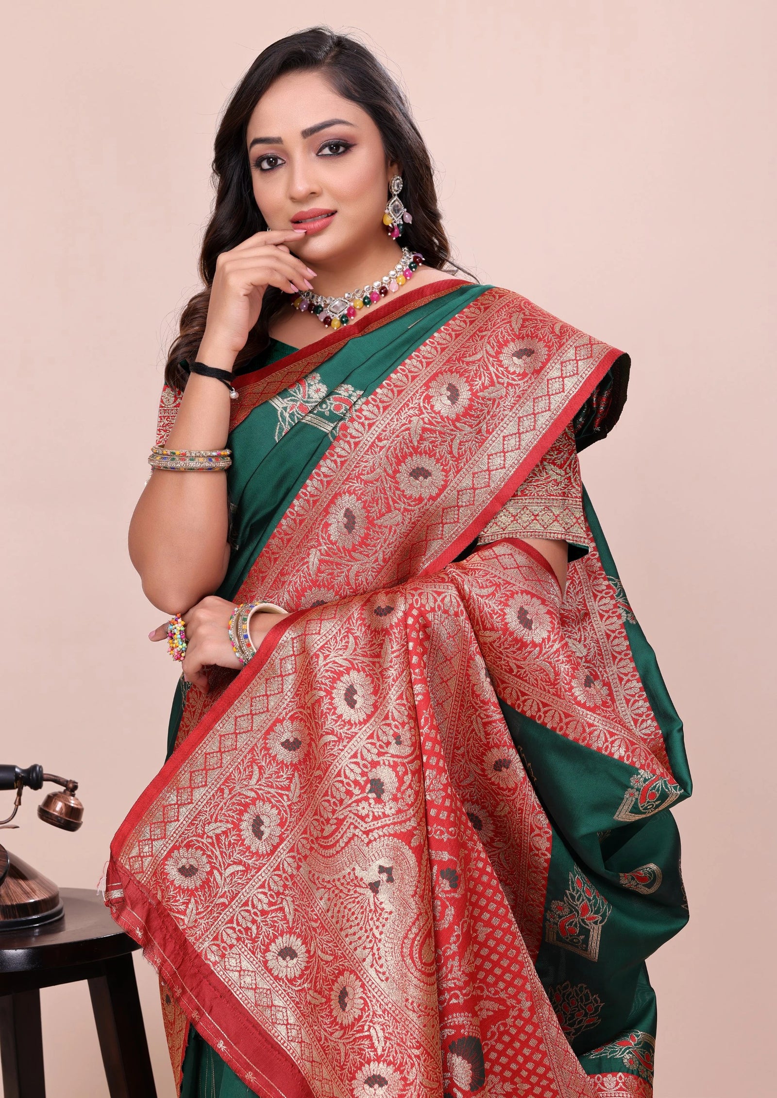 Woman wearing a green and red saree with intricate patterns on a beige background