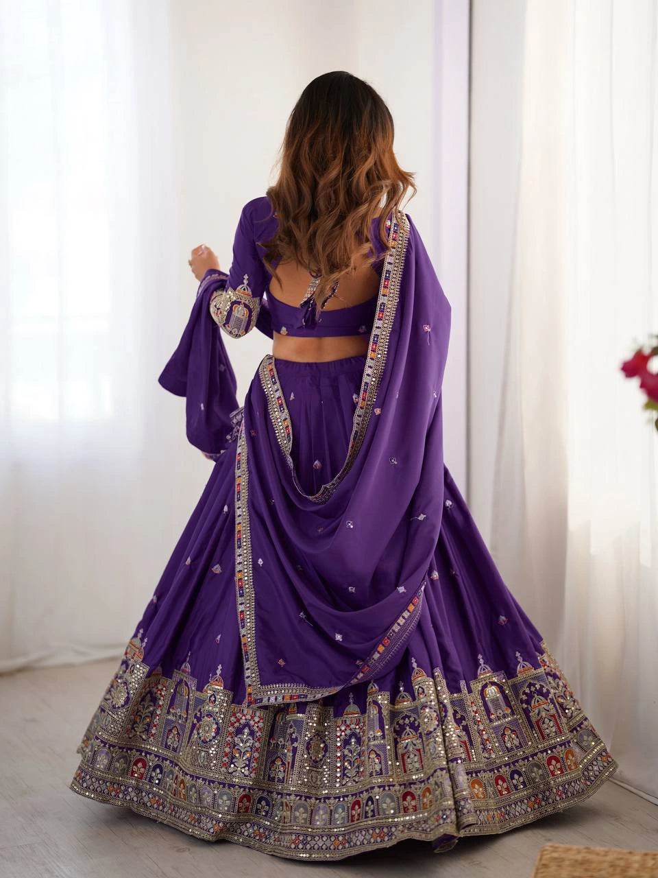 Woman wearing a purple traditional outfit with intricate designs indoors.