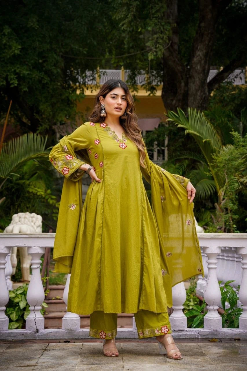 Woman in a green traditional outfit standing outdoors with greenery in the background