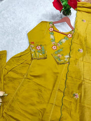 Yellow embroidered outfit on a white surface with red flowers in the background