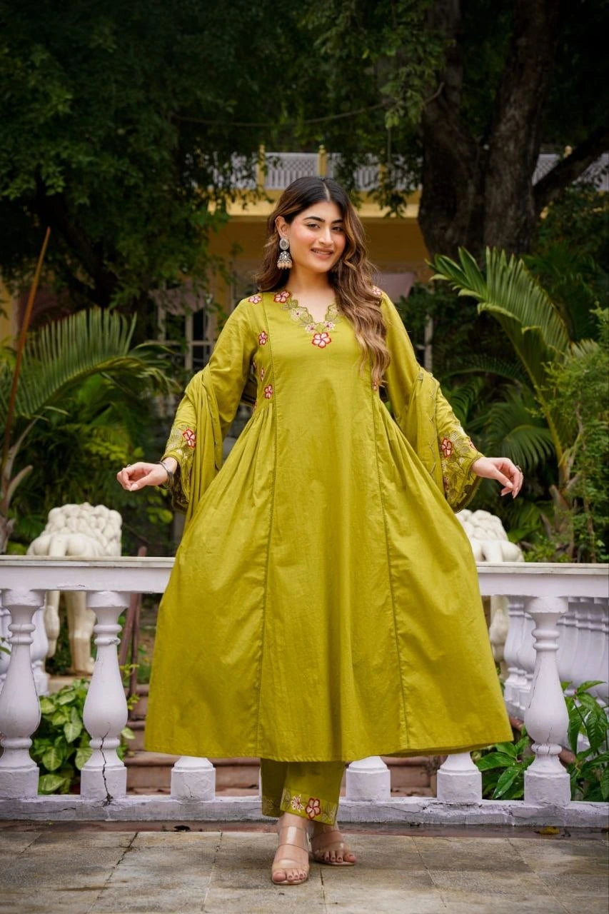 Woman in a green traditional outfit standing outdoors with greenery in the background