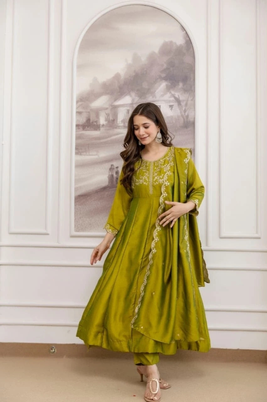Woman wearing a green traditional outfit with floral patterns in a room with white walls and a decorative mirror.