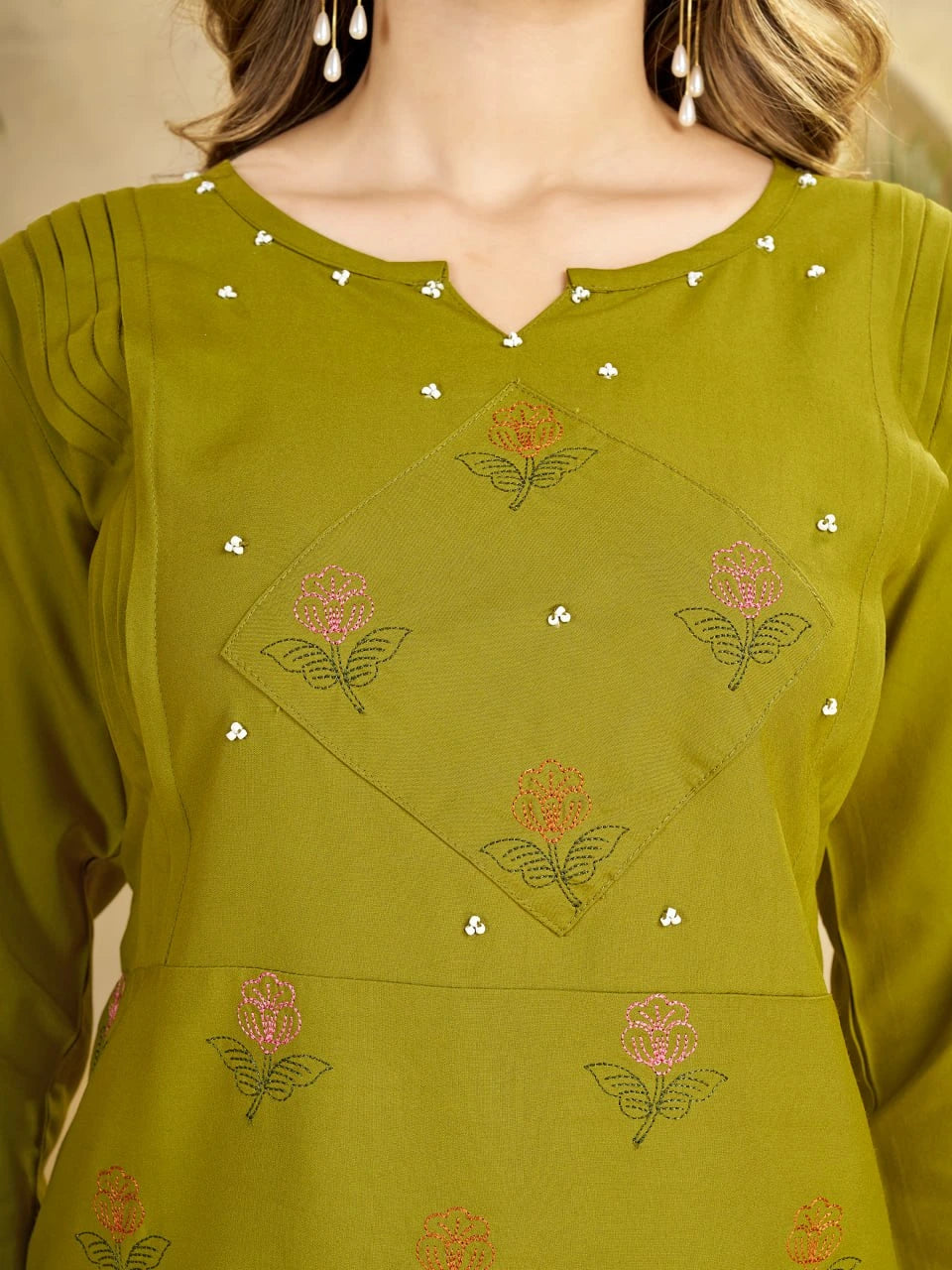 Green embroidered top with floral patterns on a neutral background