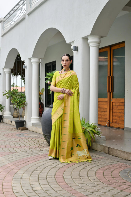 Woman in a yellow saree standing in front of a white building with arches.