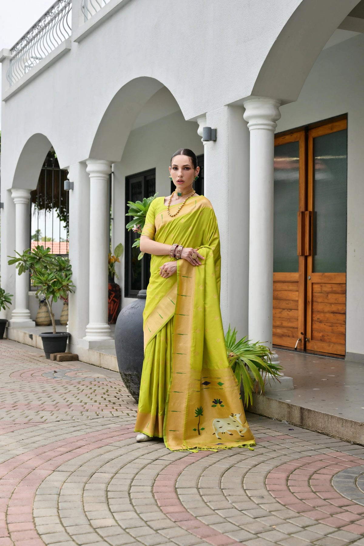 Woman in a yellow saree standing in front of a white building with arches.