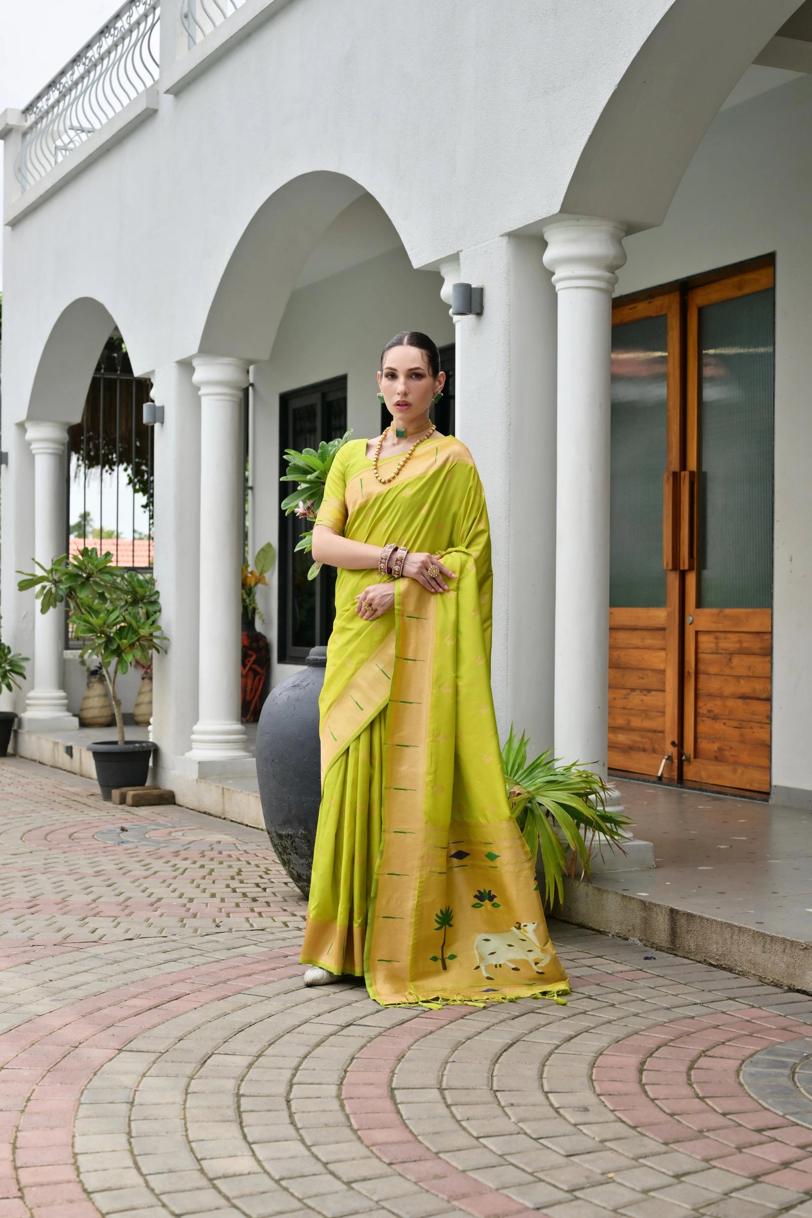 Woman in a yellow saree standing in front of a white building with arches.