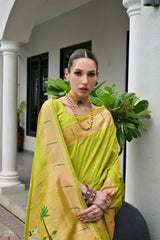 Woman in a yellow saree standing in front of a white building with greenery.