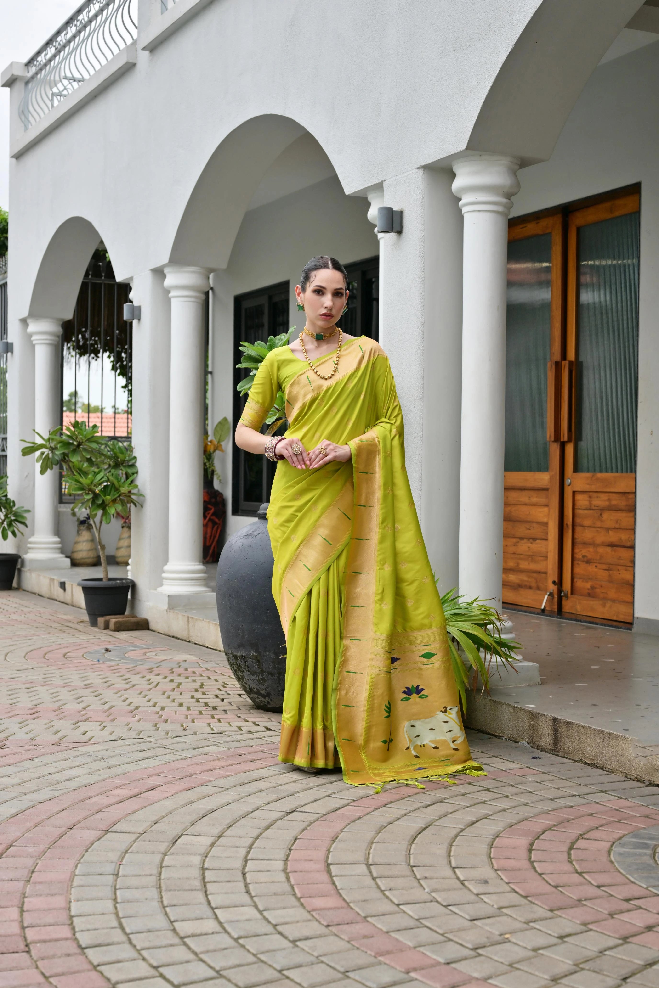 Woman in a yellow saree standing in front of a building with columns.
