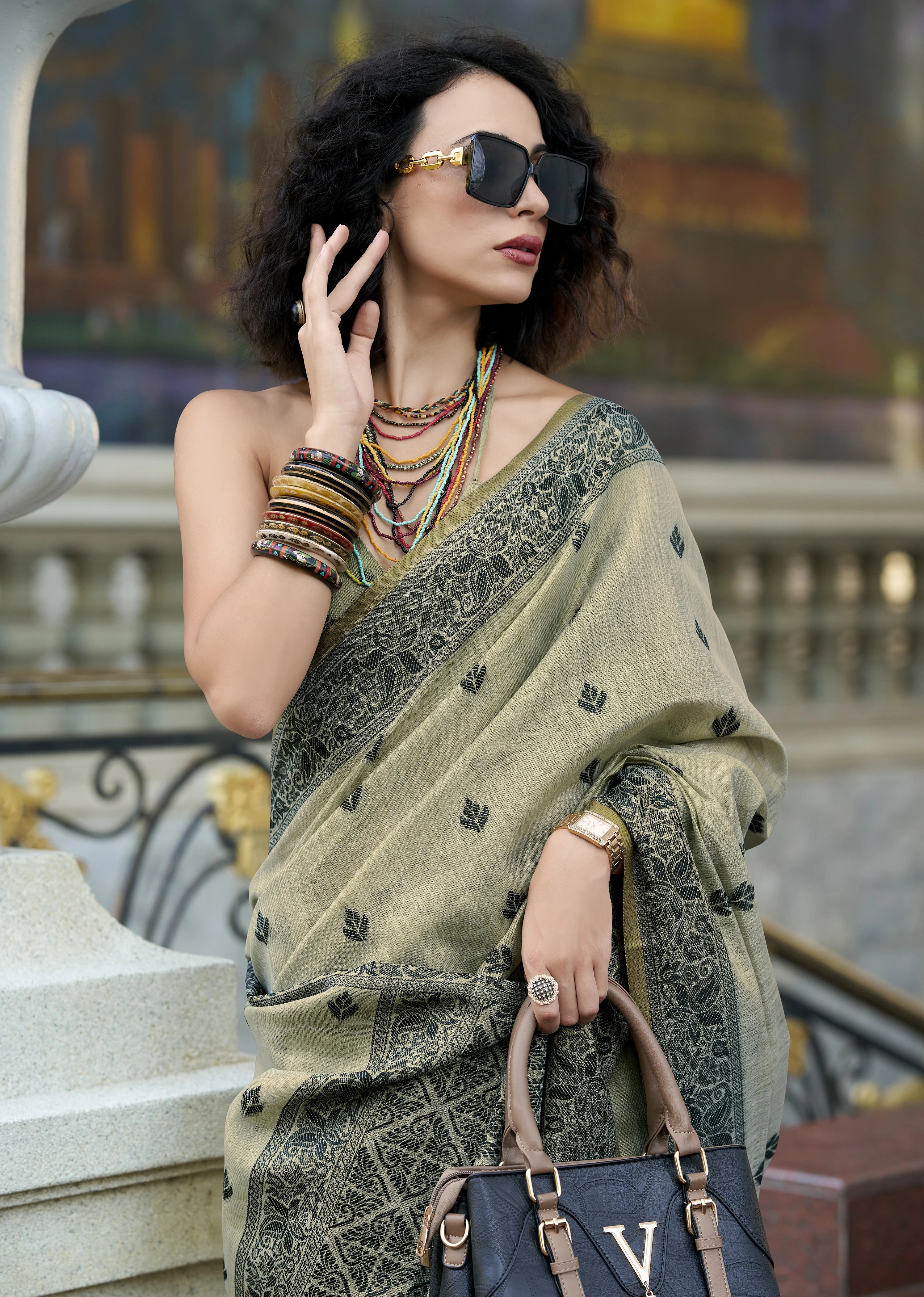 Woman in a saree with sunglasses and jewelry, standing outdoors.