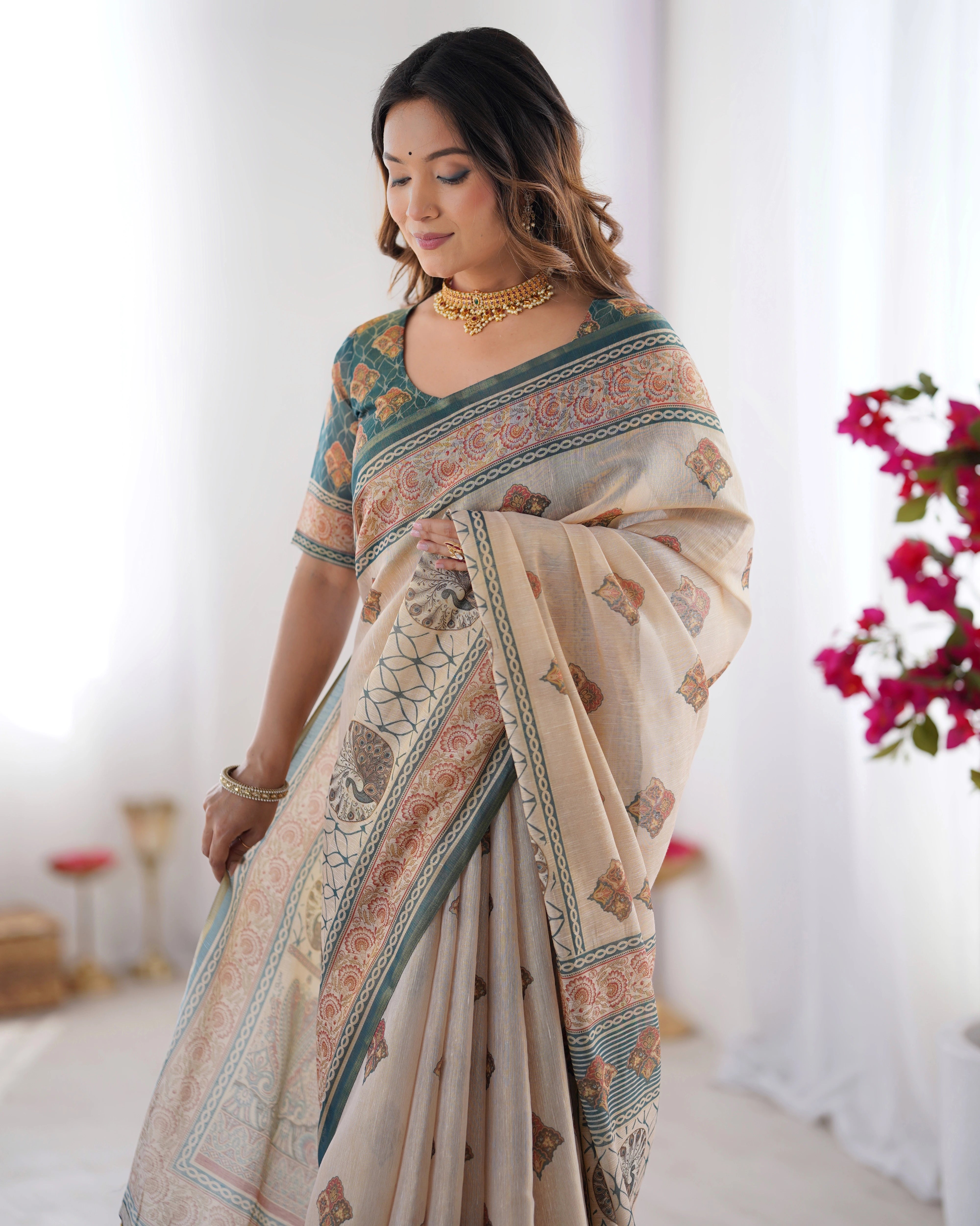 Woman in a teal saree with a beige blouse standing outdoors among greenery.