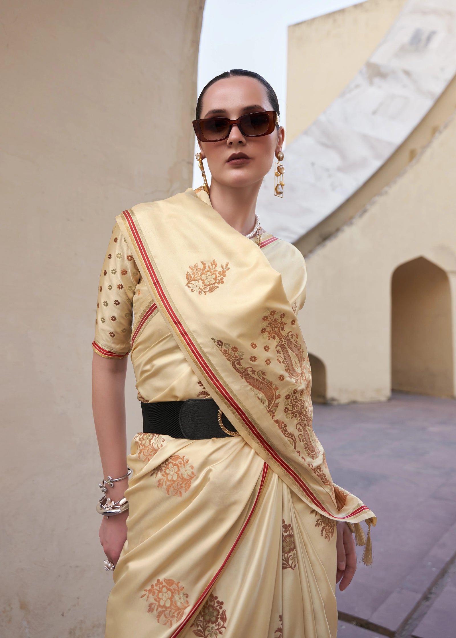 Woman wearing a traditional beige saree with red patterns in an outdoor setting.