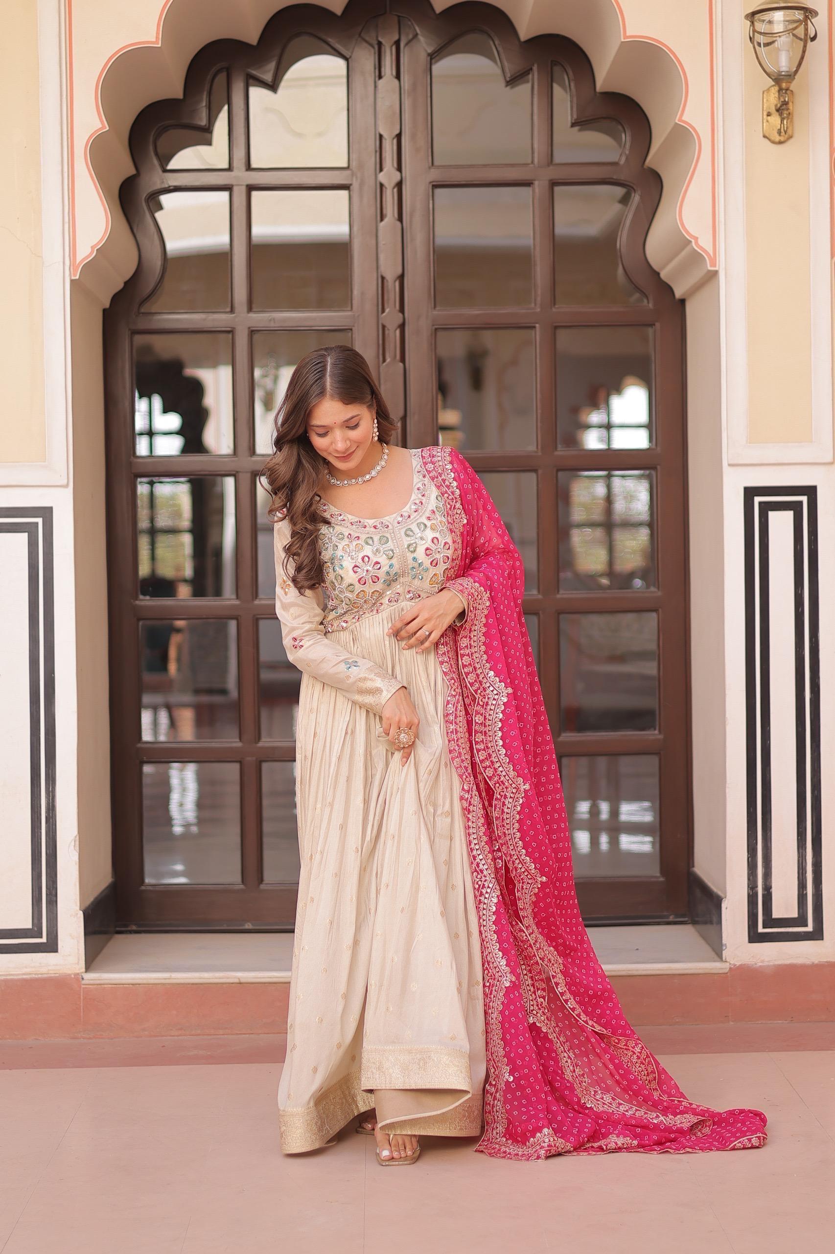 Woman in a traditional outfit with a pink dupatta standing in front of an ornate door.