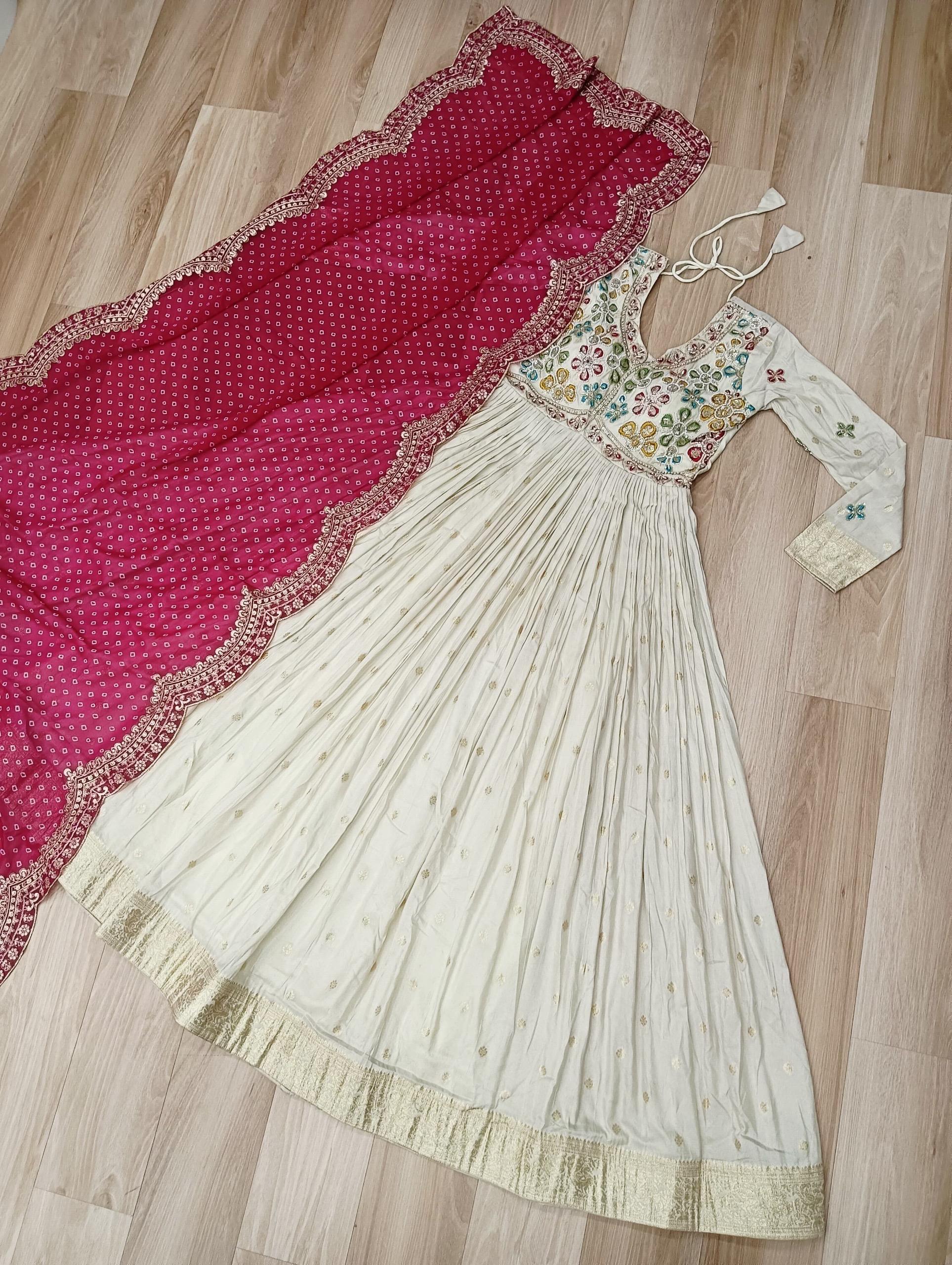 White traditional dress with floral patterns and a red dupatta on a wooden floor.