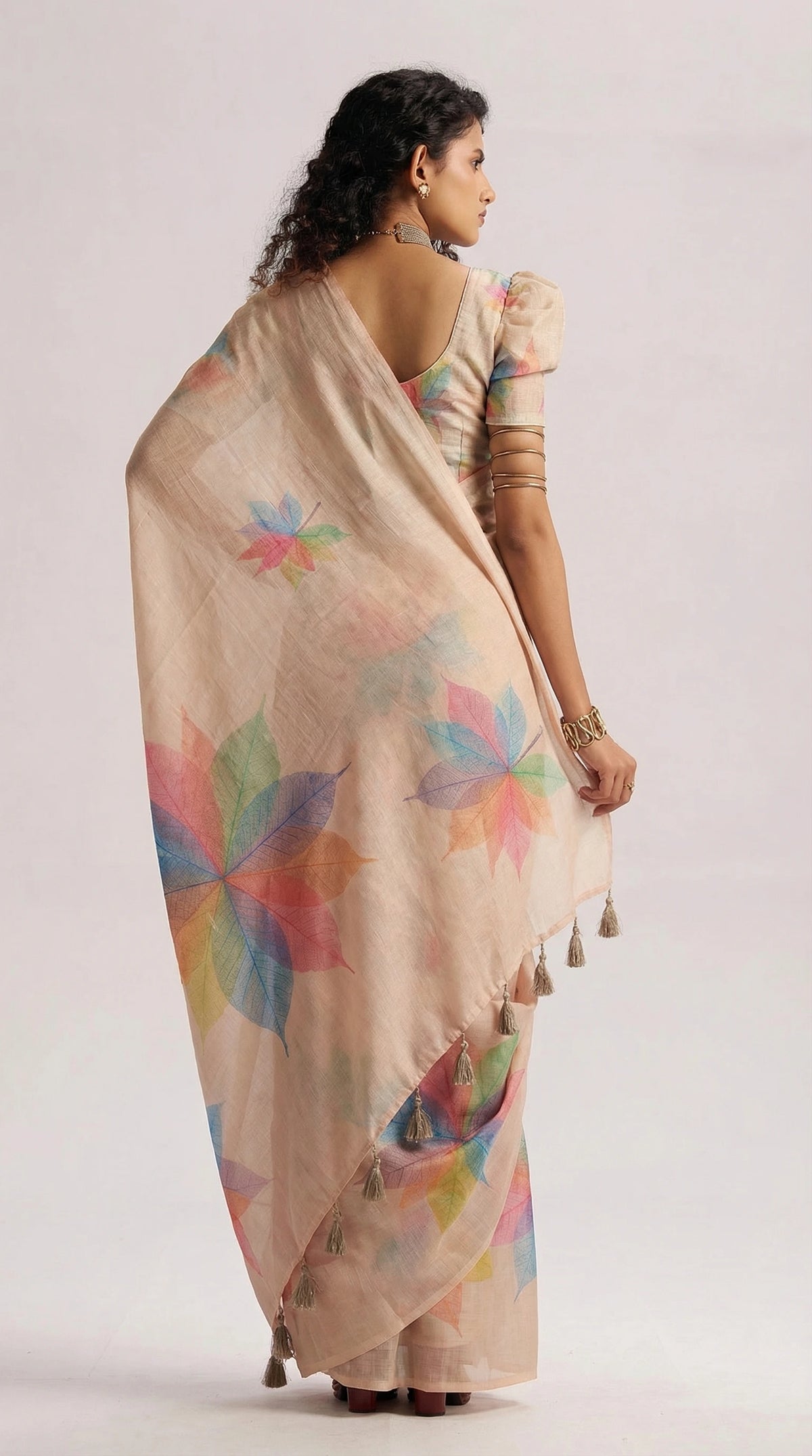 Woman wearing a beige saree with colorful floral patterns on a plain background
