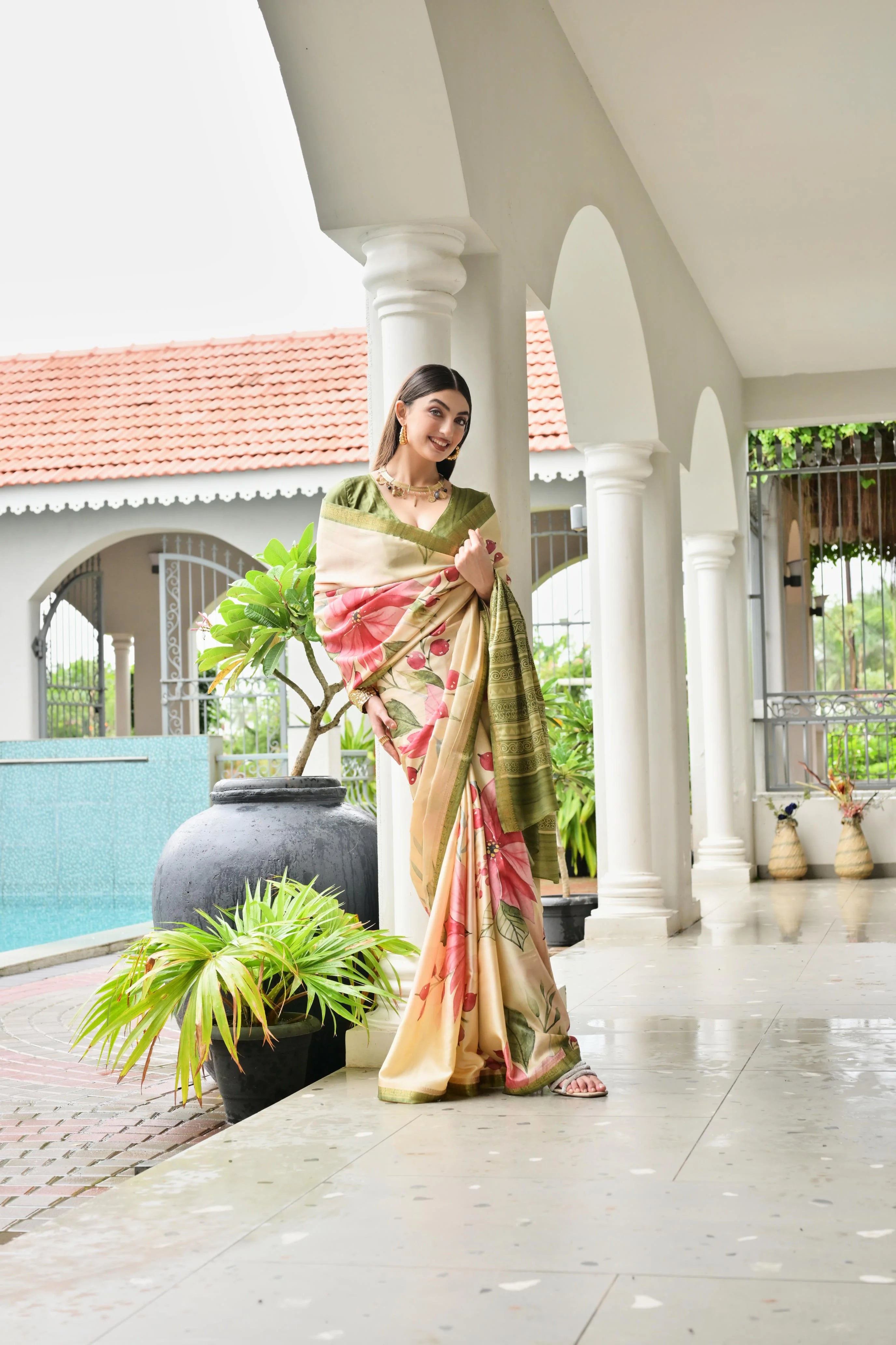 Woman in a traditional saree standing in a decorative outdoor setting with columns and plants.