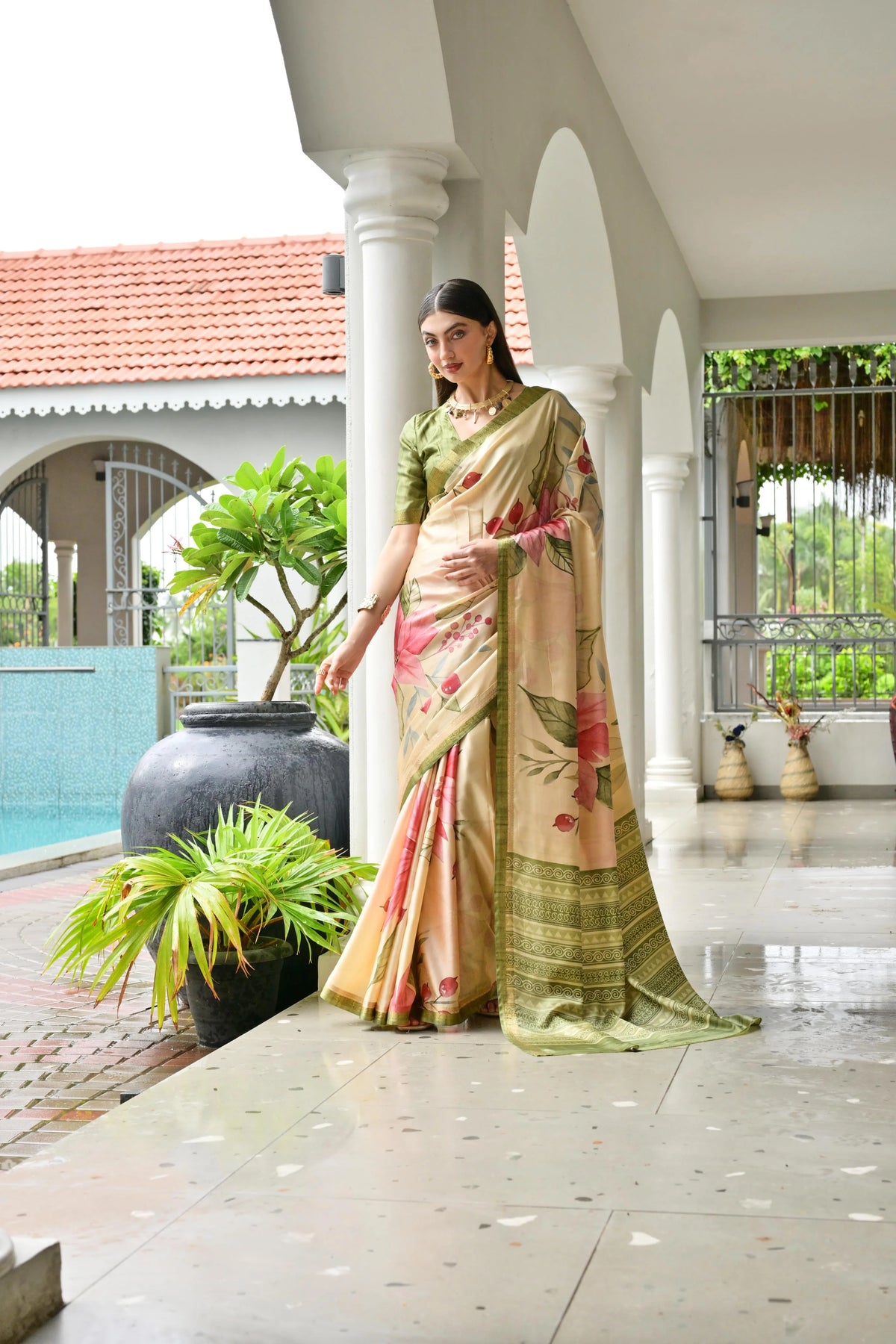 Woman in a traditional saree standing on a porch with plants and a pool in the background