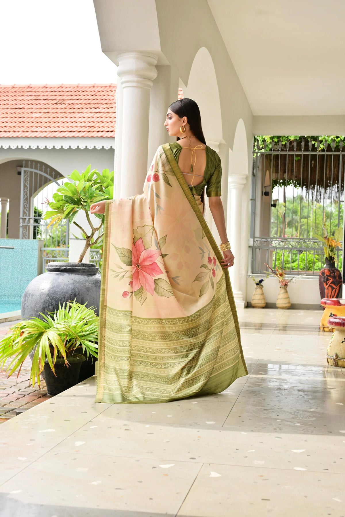 Woman in a green saree with floral design standing in a well-lit outdoor setting.