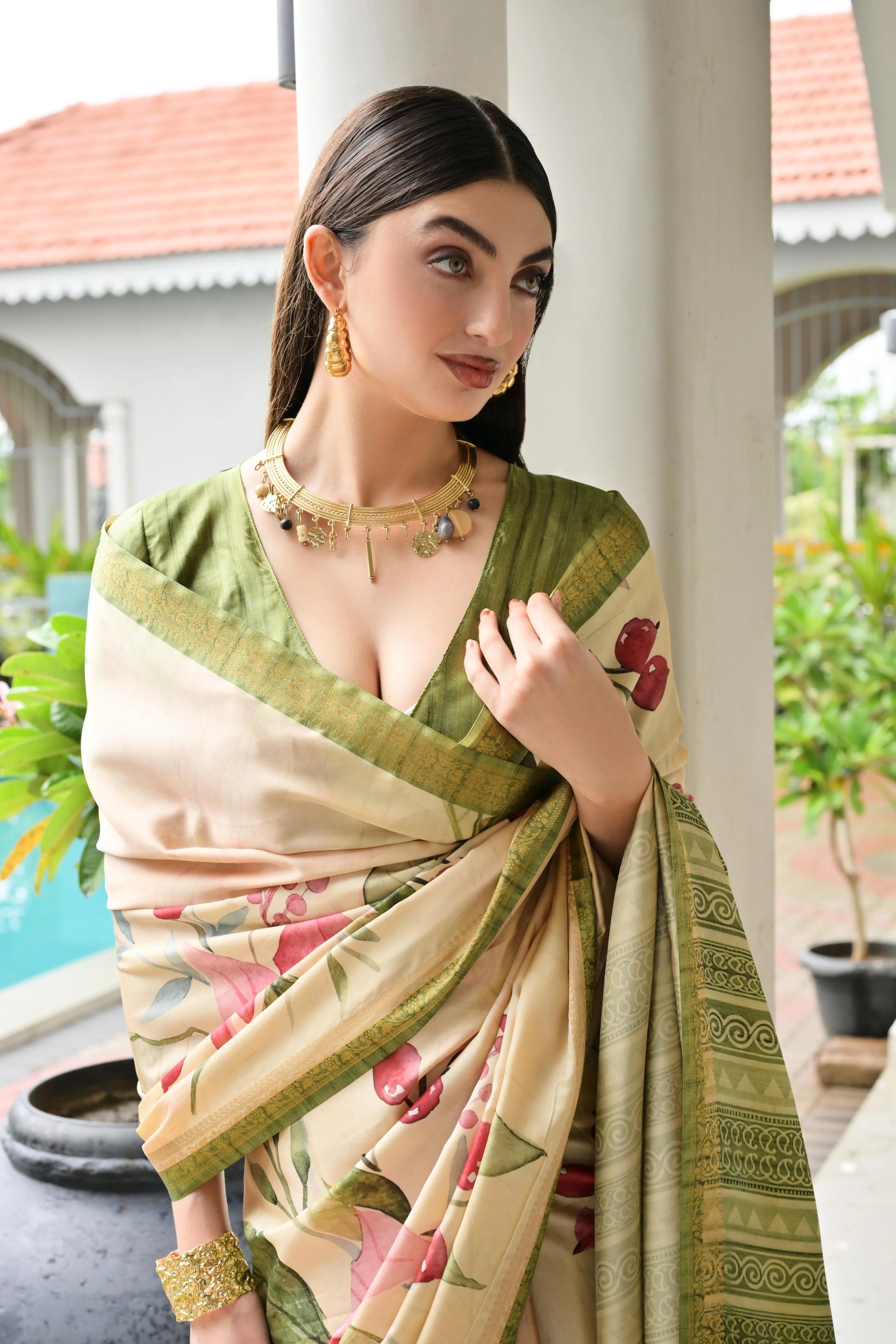 Woman wearing a green and beige saree with floral patterns, standing outdoors.
