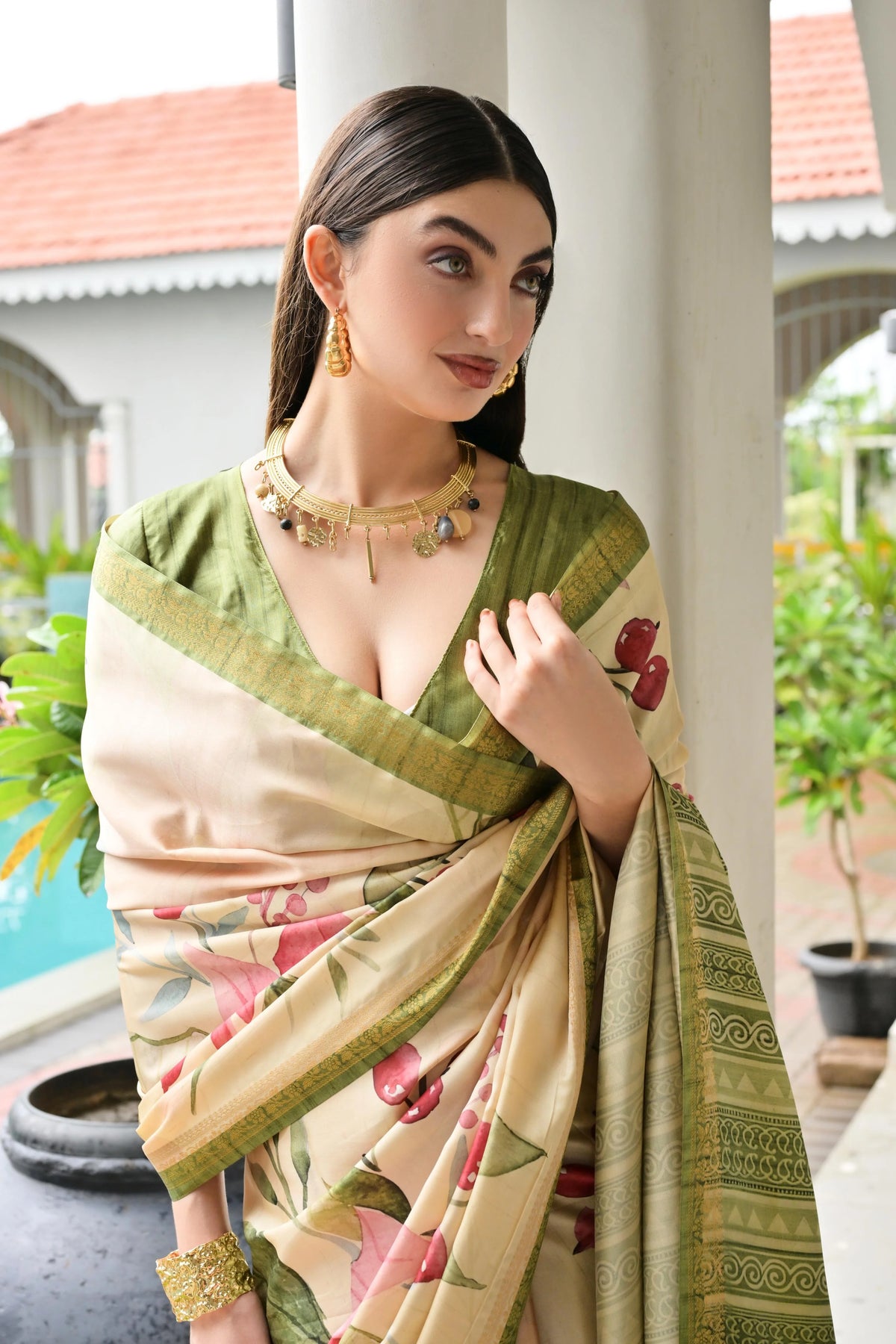 Woman wearing a green and beige saree with floral patterns, standing outdoors.