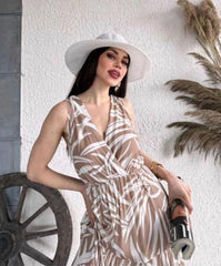 Woman in a patterned dress and wide-brimmed hat against a white wall with decorative elements.