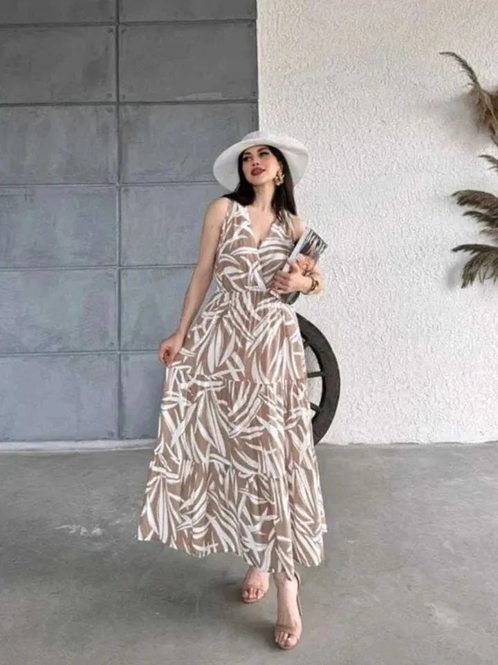Woman in a patterned dress and white hat standing against a concrete wall.