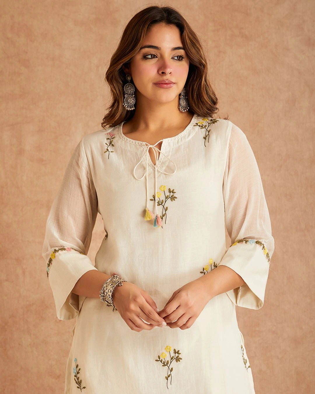 Woman wearing a cream-colored embroidered dress against a beige background