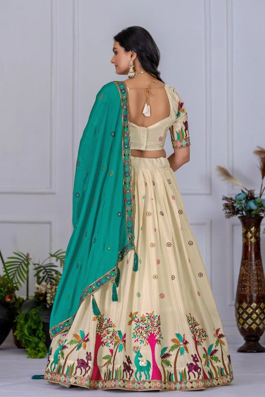 Woman wearing a traditional cream saree with green blouse and floral patterns, standing against a white paneled wall.