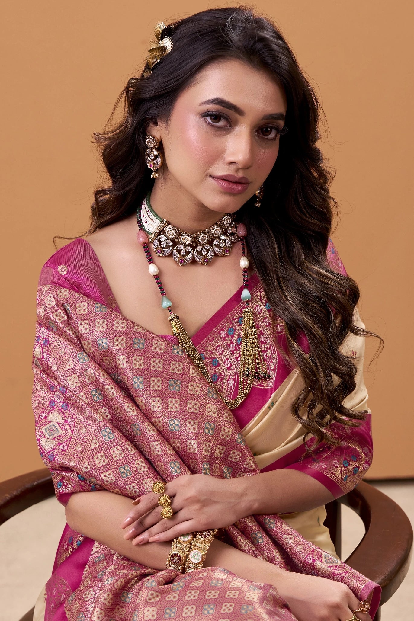 Woman in traditional pink and gold saree with jewelry against a beige background