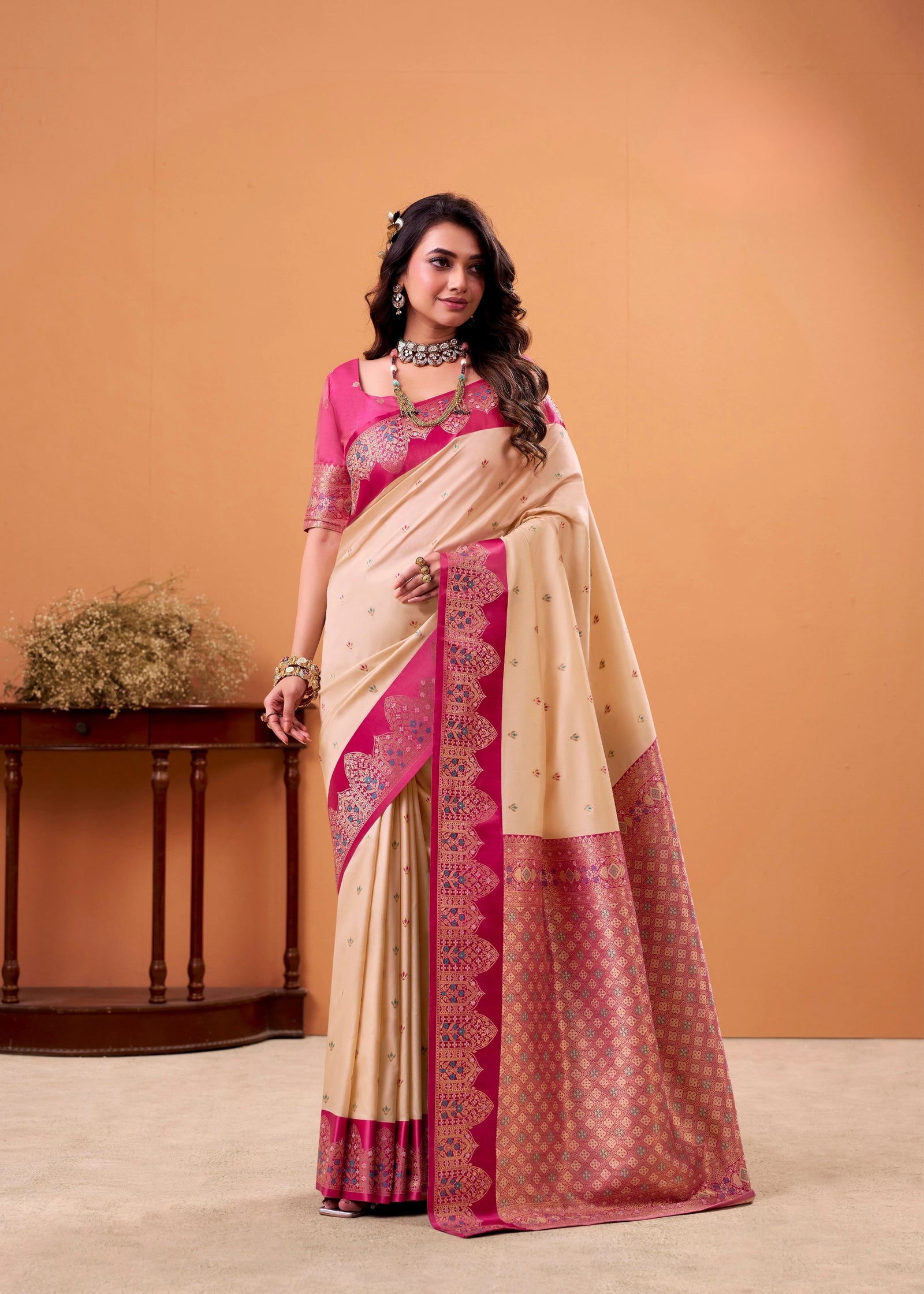 Woman wearing a beige and pink saree against an orange background
